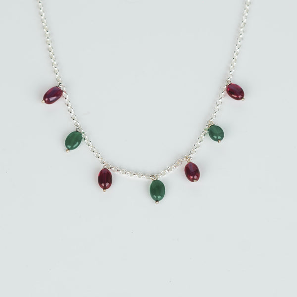 Model wearing silver necklace with red and green gemstone beads
