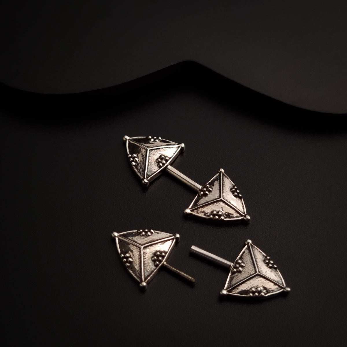 a pair of triangle shaped earrings on a black surface