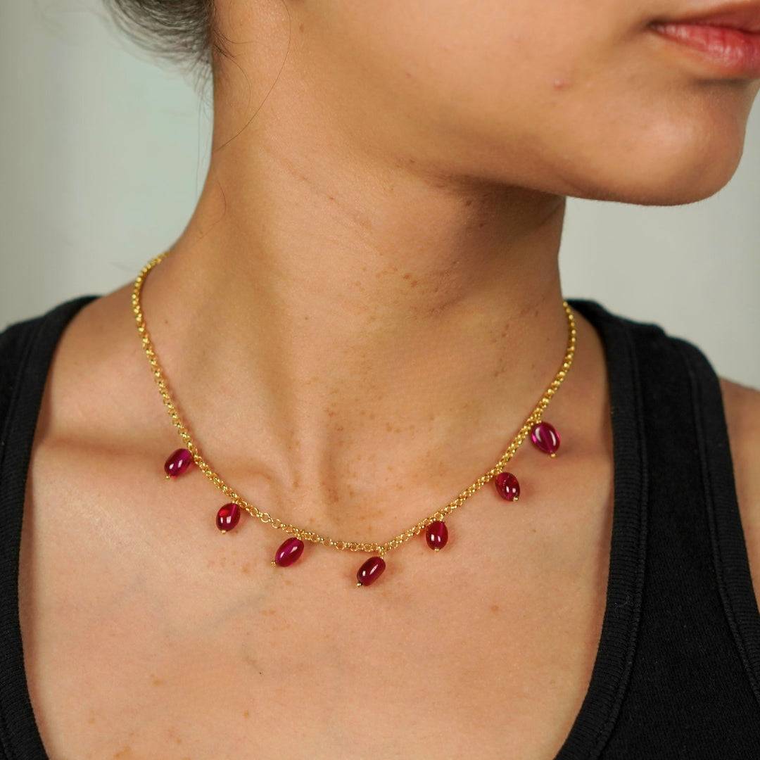 Model wearing gold necklace with ruby beads