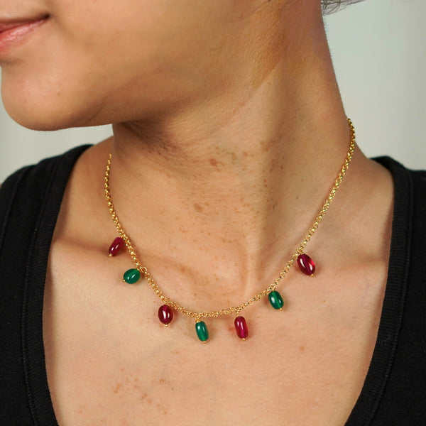 Model wearing gold chain with red and green gemstone beads for elegant look