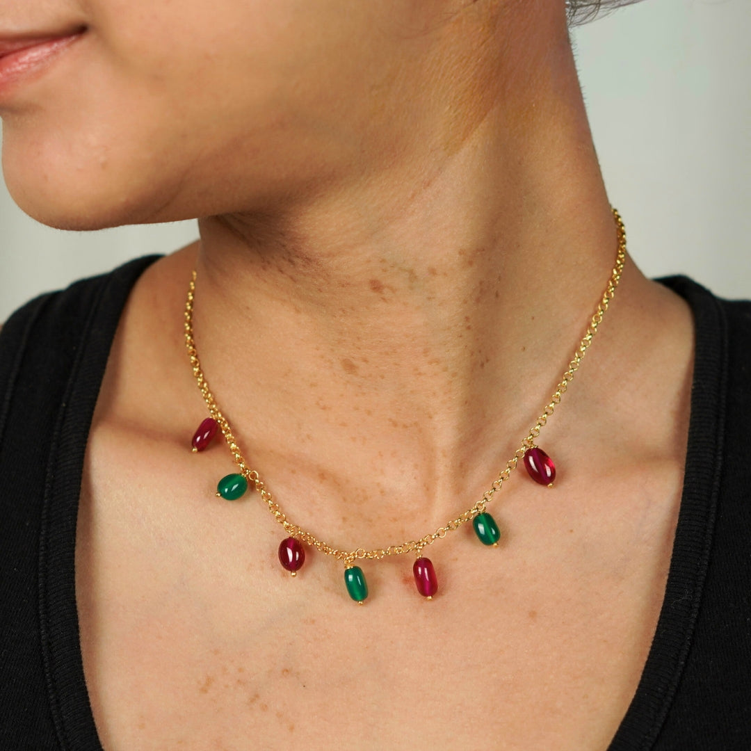 Model wearing gold chain with red and green gemstone beads for elegant look