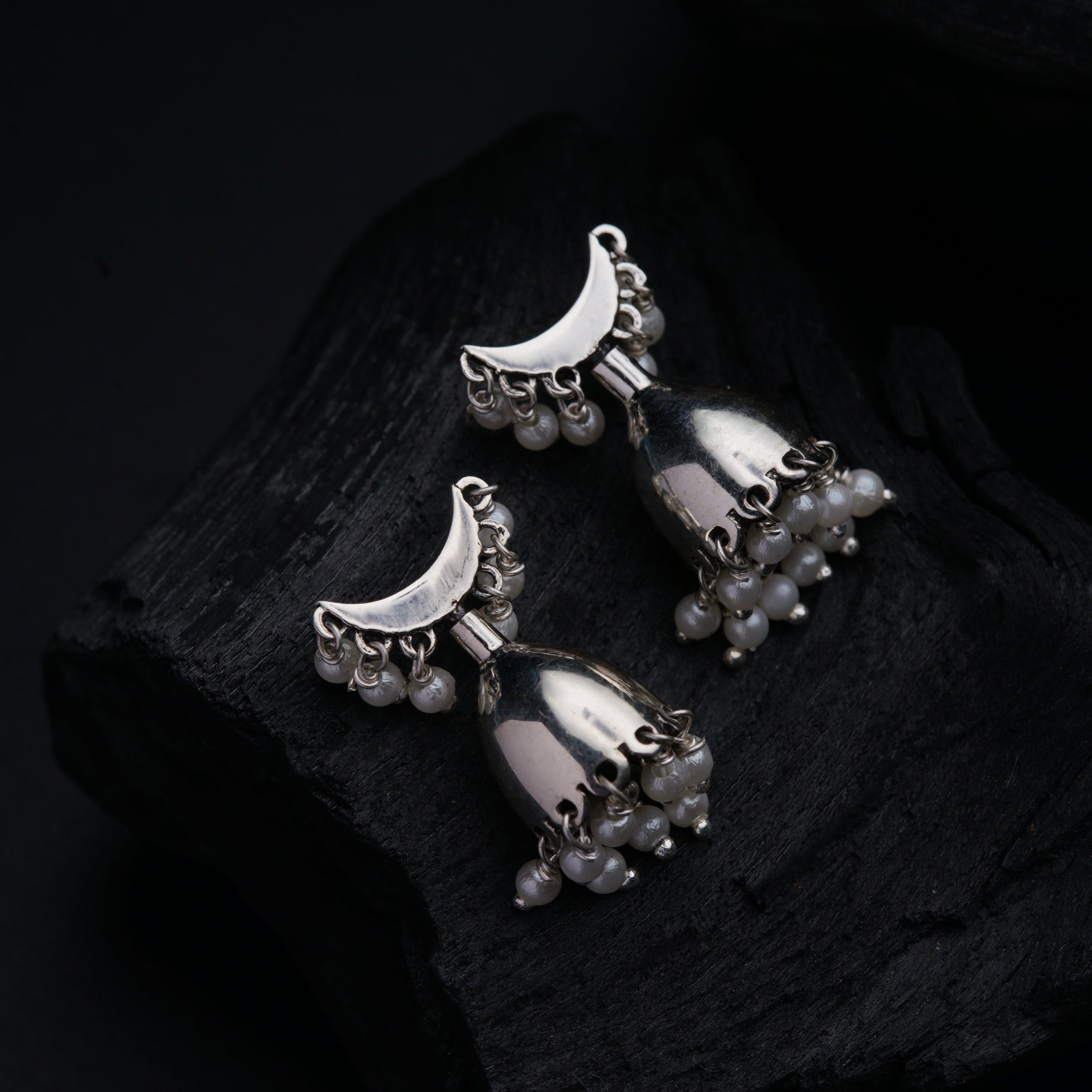 a pair of silver toned earrings on a piece of wood