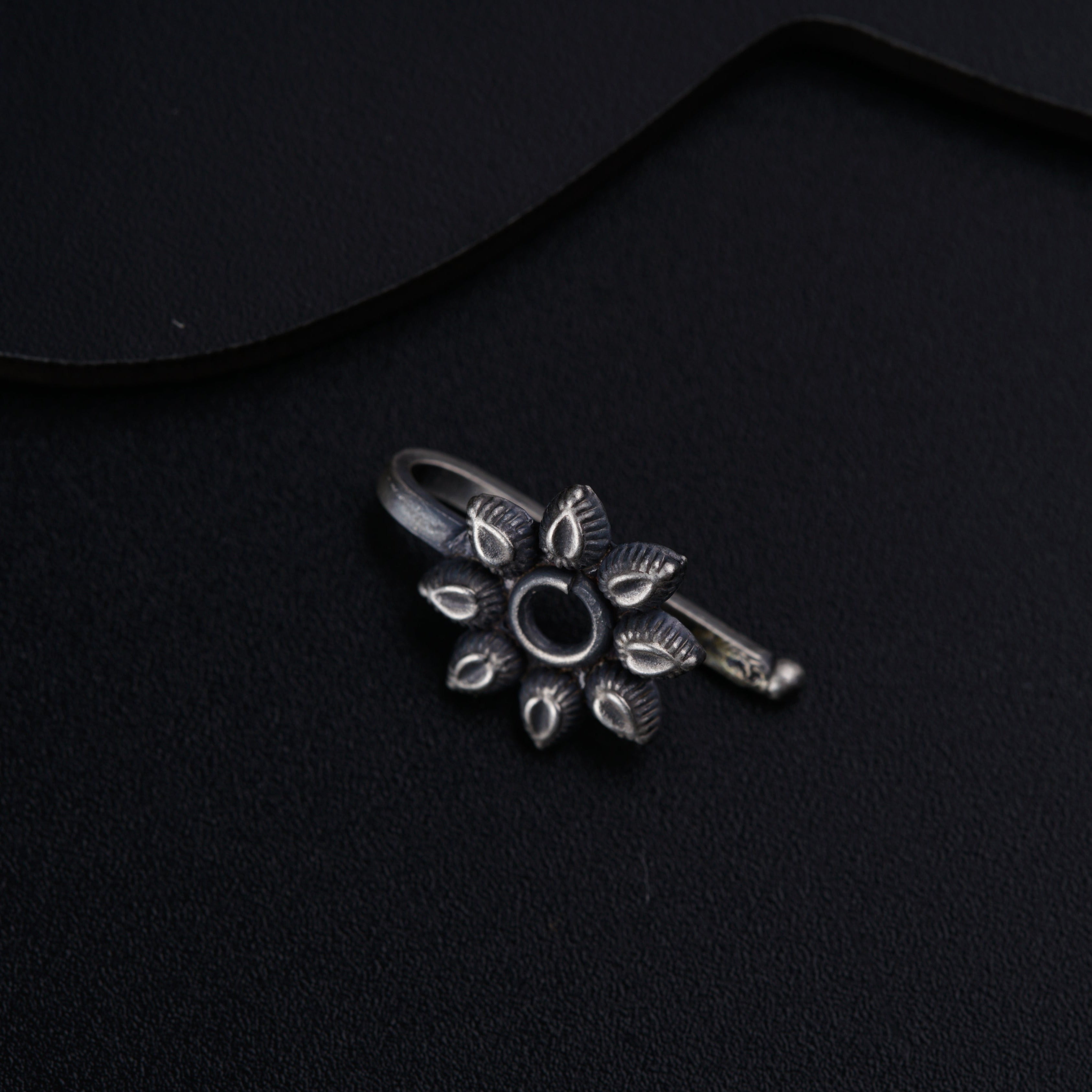 a silver ring with a flower design on a black surface