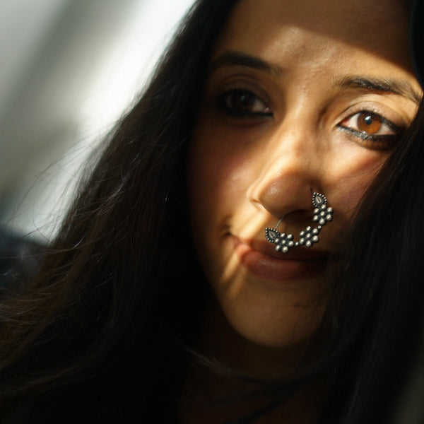 Close-up of a woman wearing a traditional silver nose ring with floral design, brown eyes, and dark hair