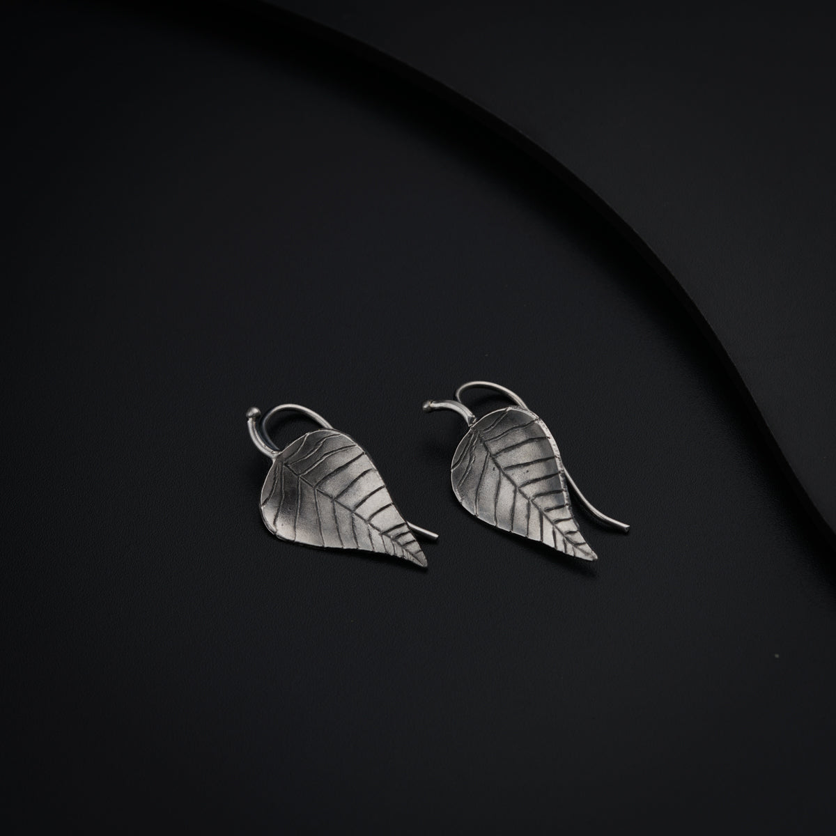 a pair of silver leaf earrings on a black surface