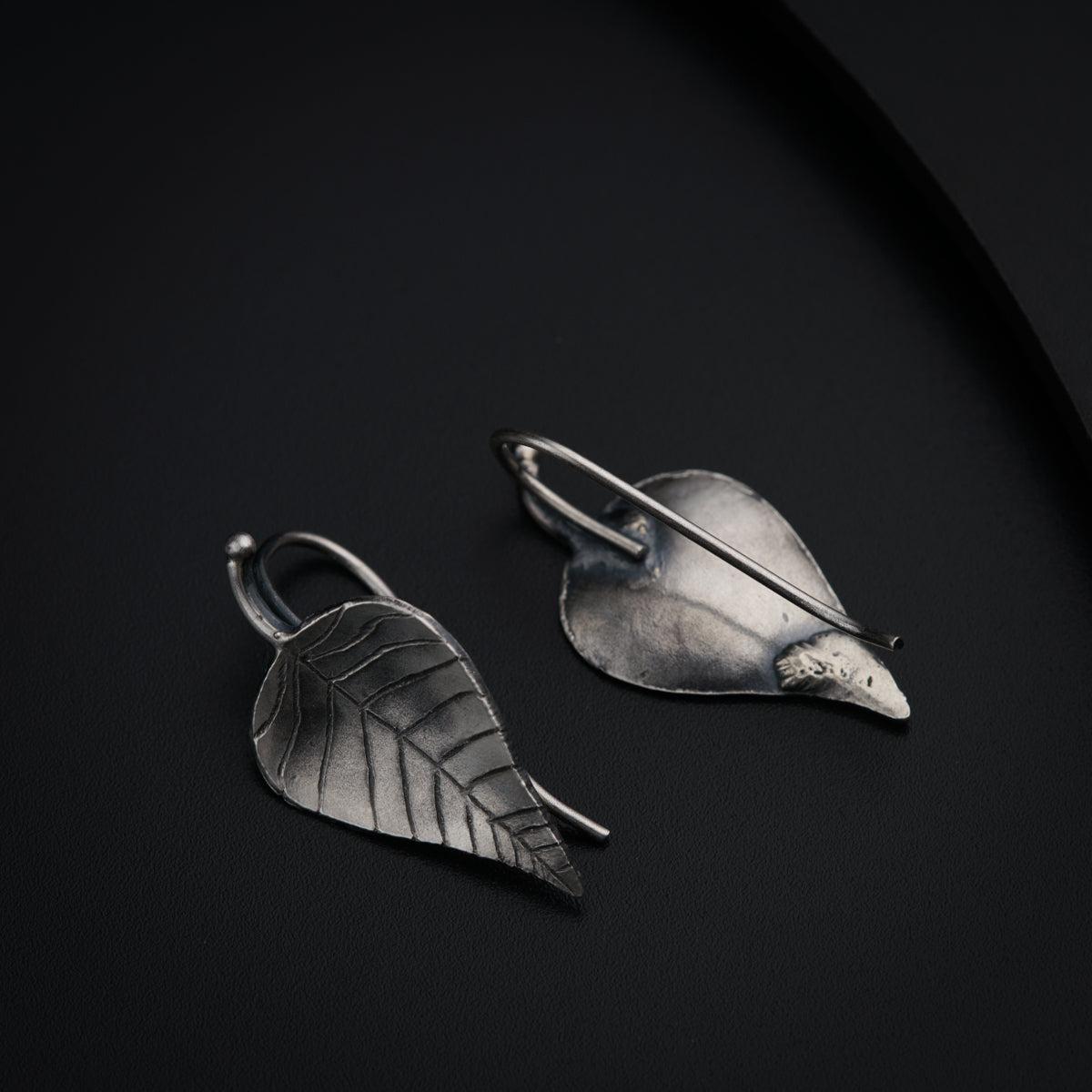a pair of silver leaf earrings on a black surface