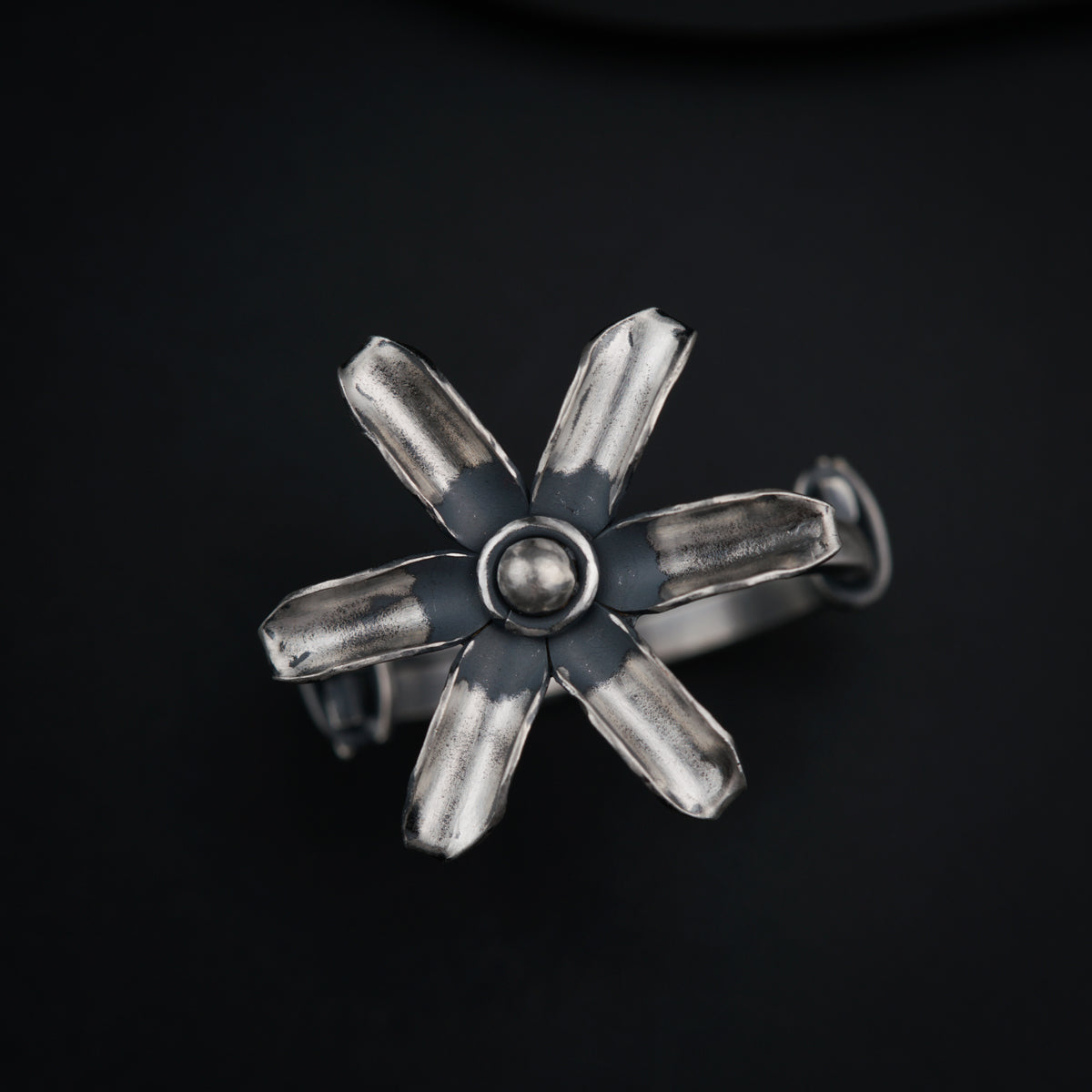 a silver ring with four petals on a black surface