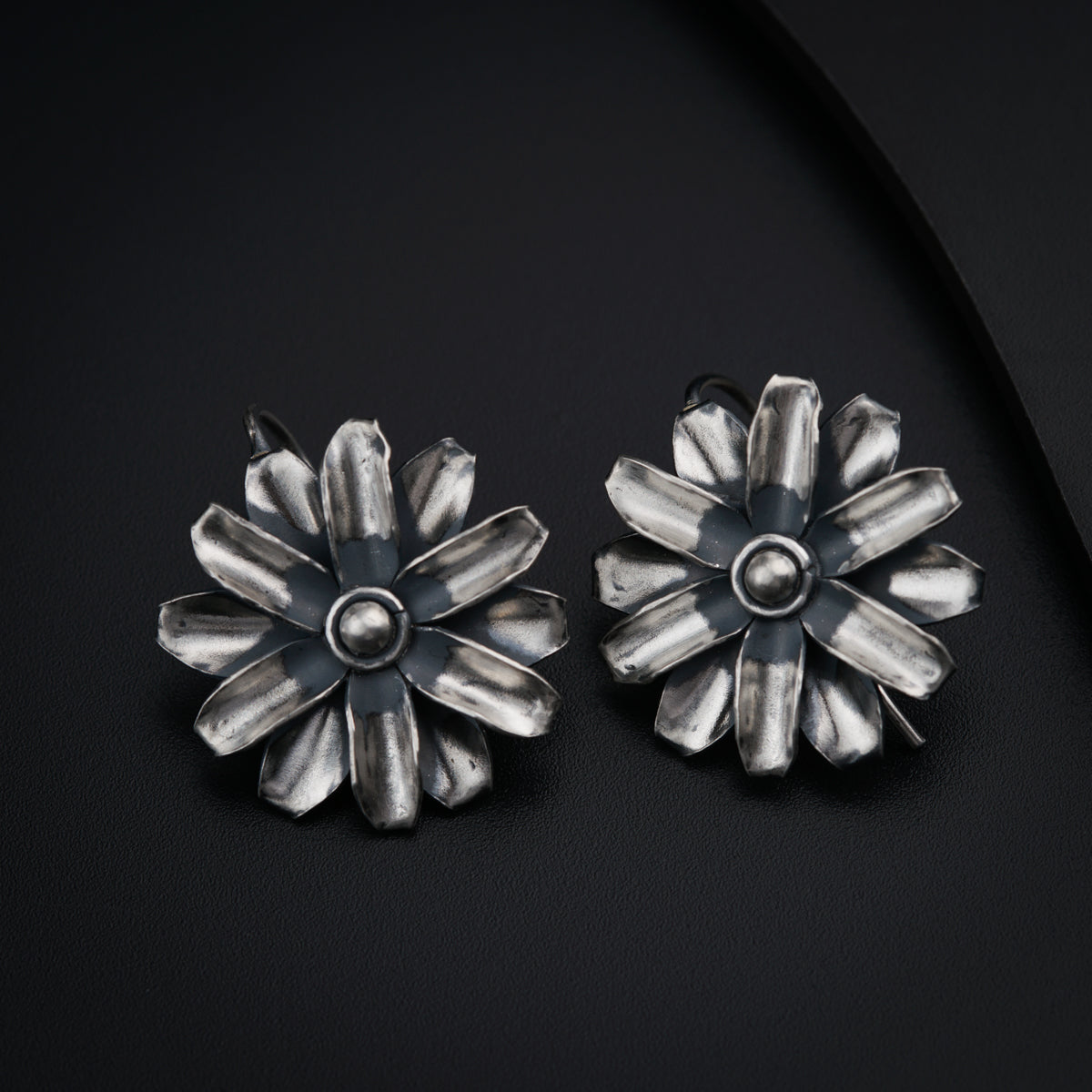 a pair of silver flower shaped earrings on a black surface