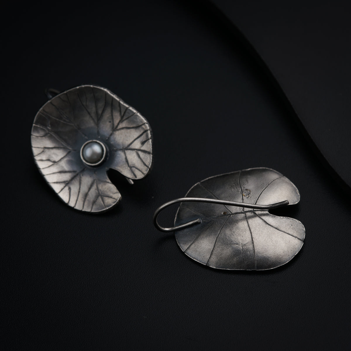 a pair of silver earrings with leaves on a black background