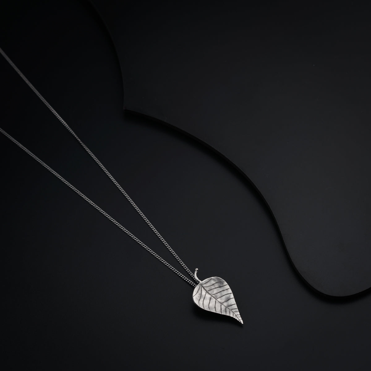 a silver necklace with a leaf on a black background