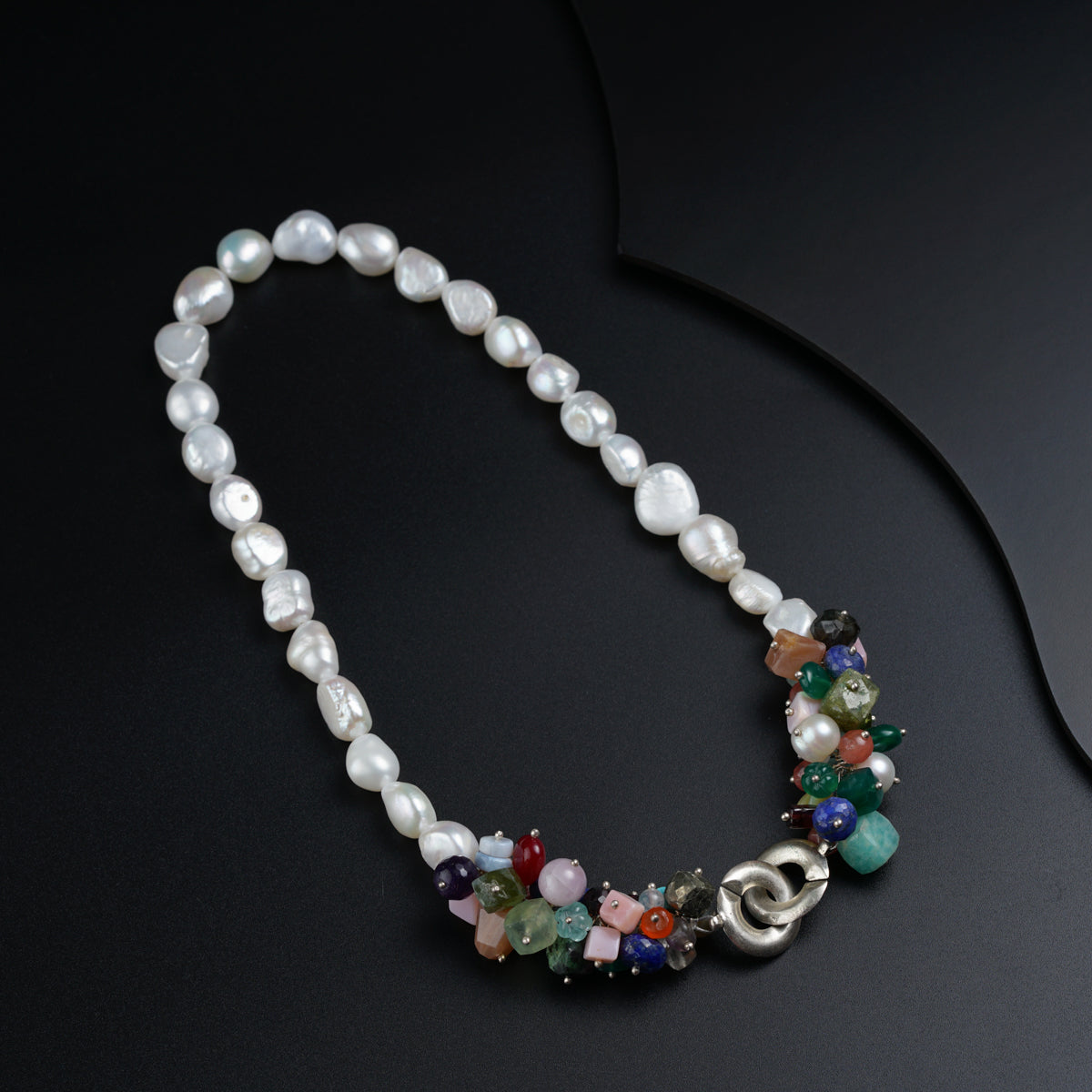 a necklace with pearls, beads, and charms on a black surface
