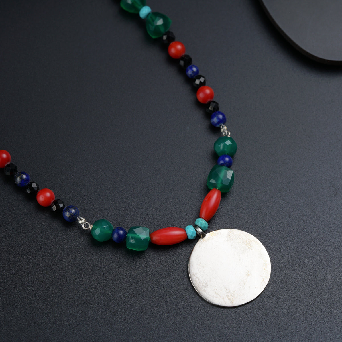a necklace with beads and a disc on a table