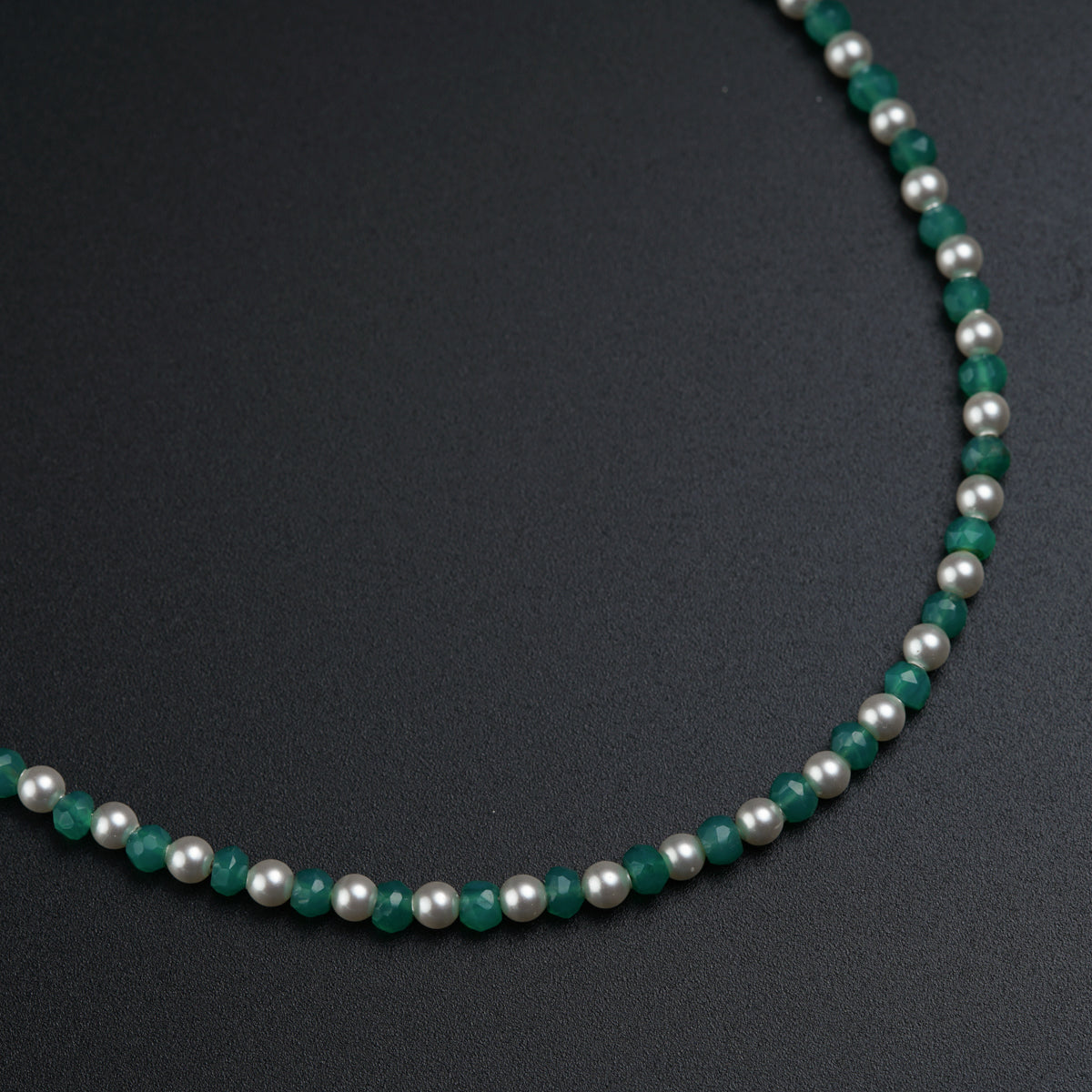 a necklace with pearls and green beads on a black surface