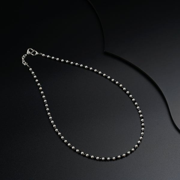 a silver beaded necklace on a black surface