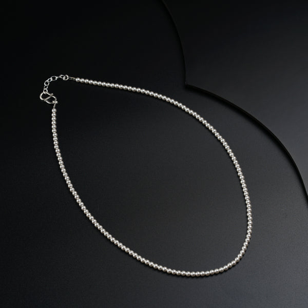 a silver necklace with a white bead on a black background