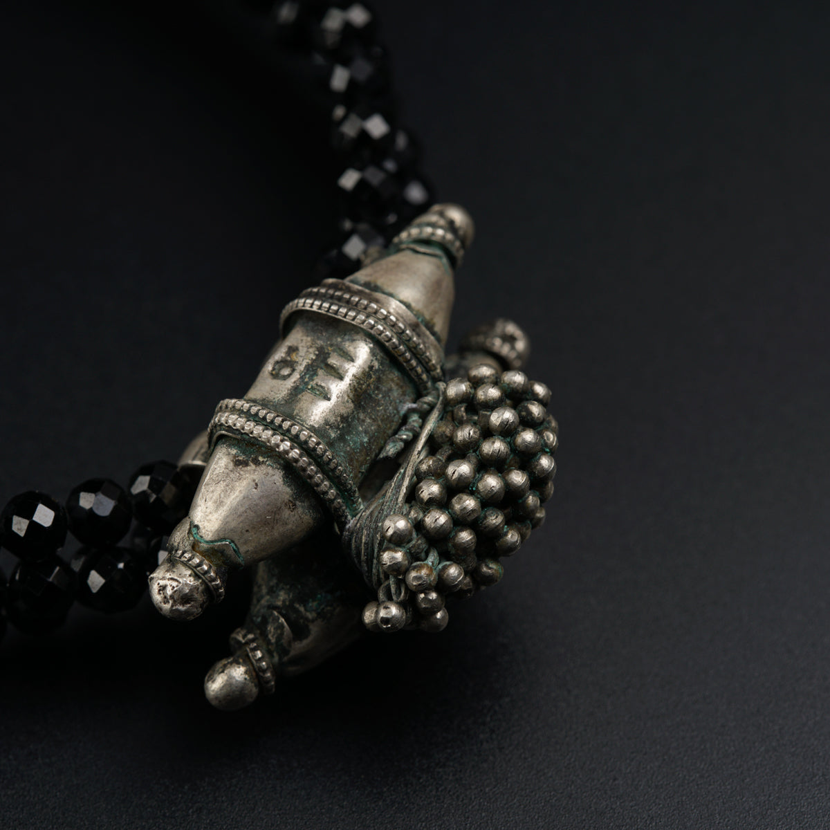 a black beaded necklace with a silver object on it