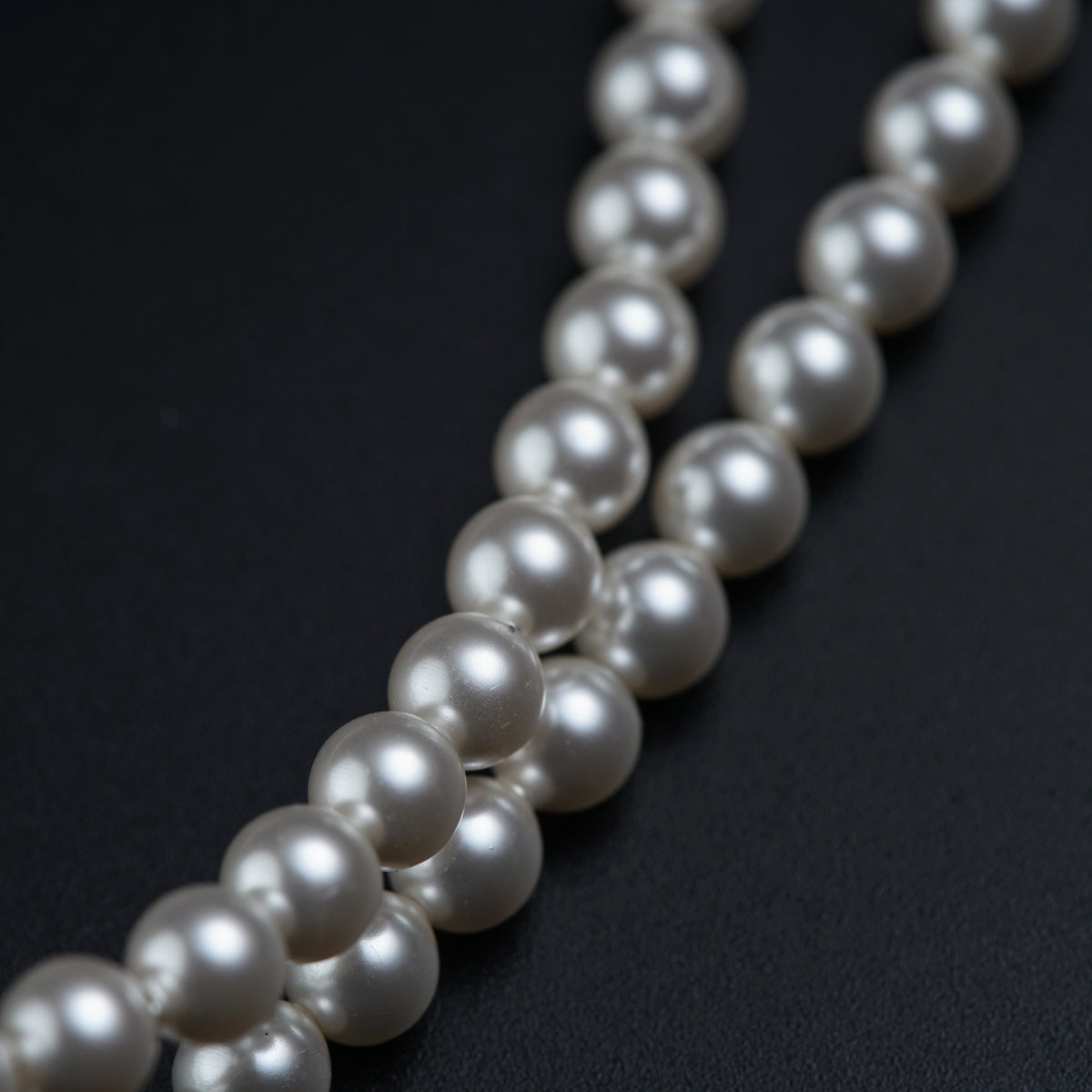 a long strand of white pearls on a black surface