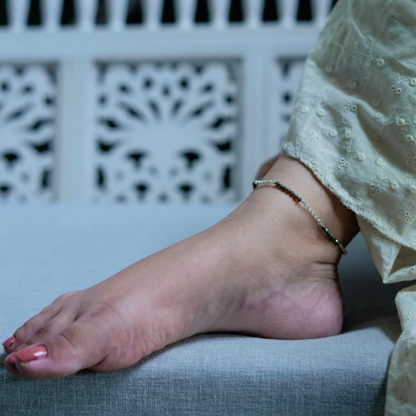 Close-up of anklet chain with black beads on white fabric
