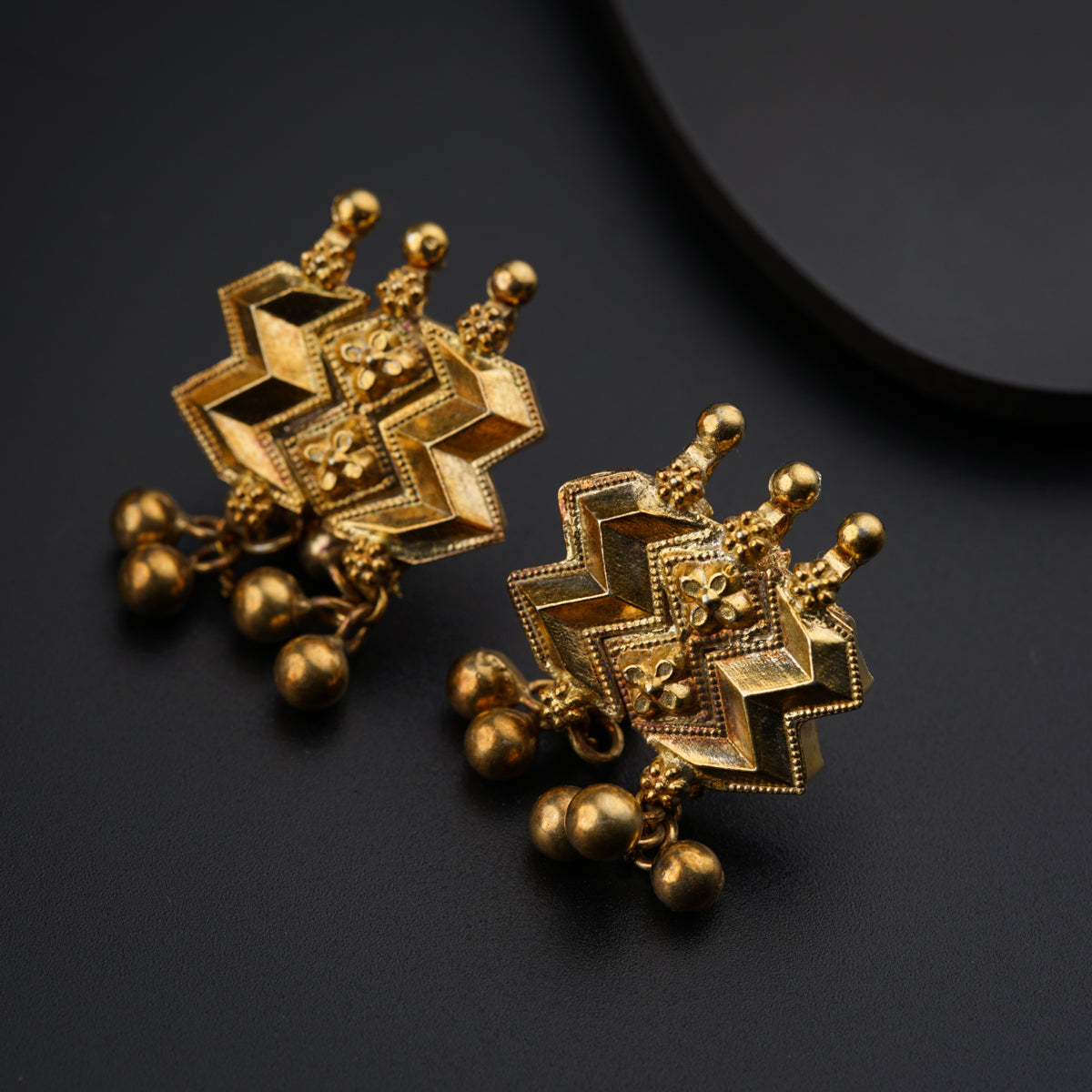 a pair of gold earrings on a black surface