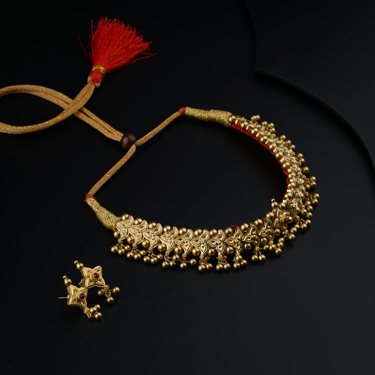 a gold necklace and a red tassel on a black surface