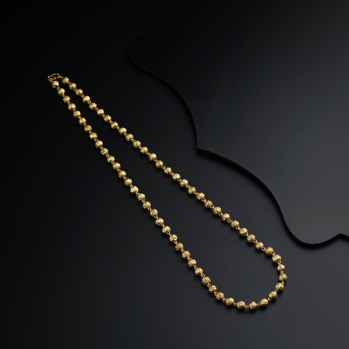 a gold beaded necklace on a black surface