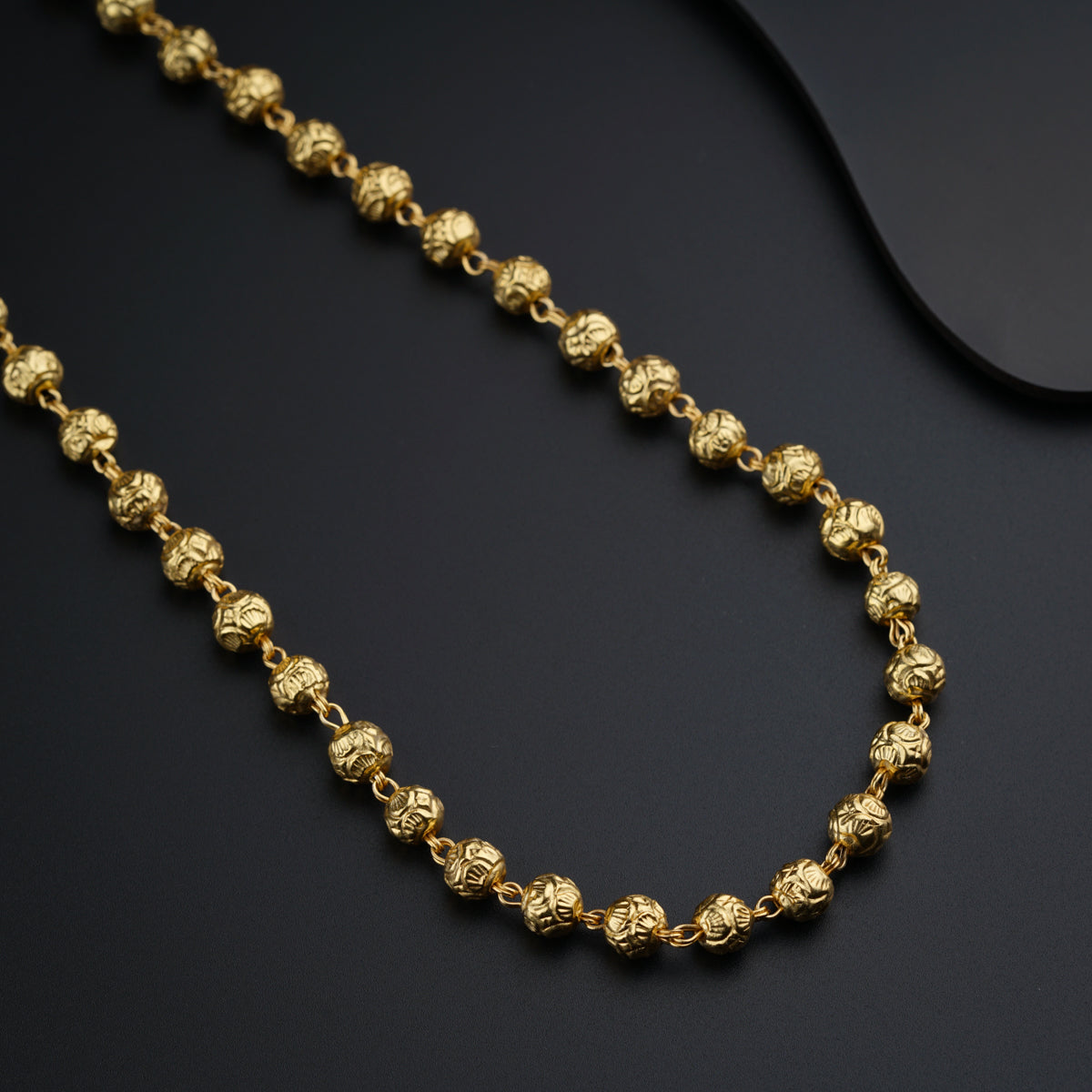 a gold beaded necklace on a black surface