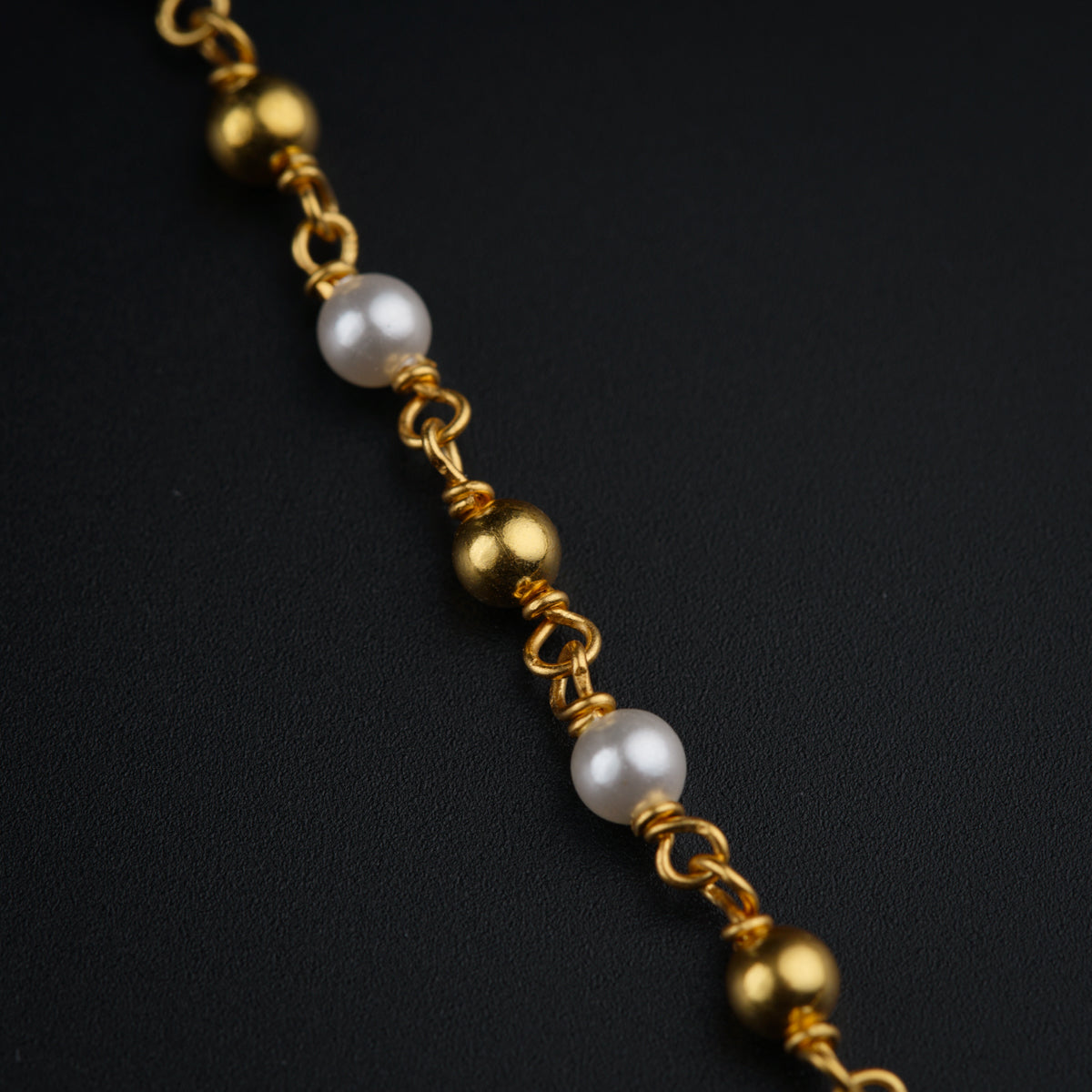 a close up of a gold chain with pearls