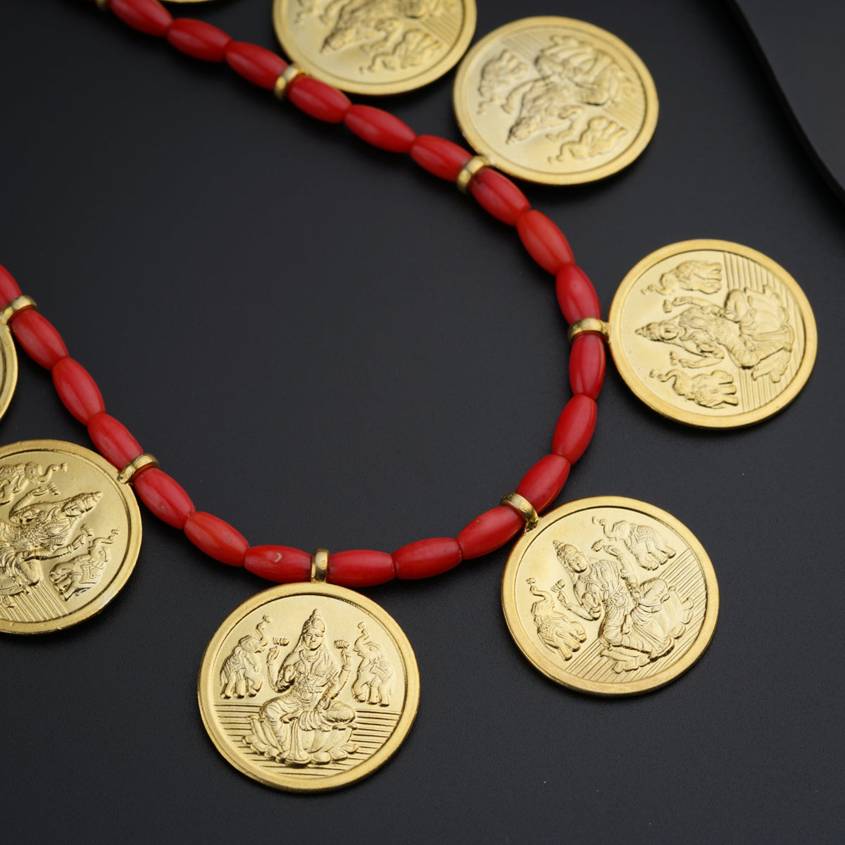 a red beaded necklace with gold coins on a black surface