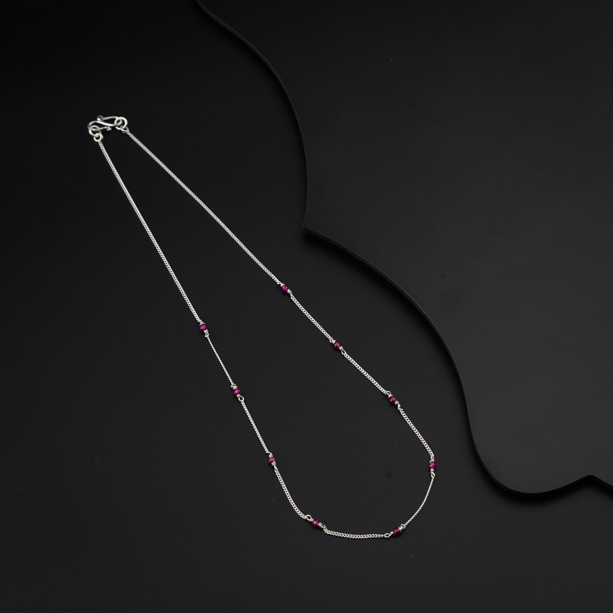 a silver necklace with a red bead on a black background