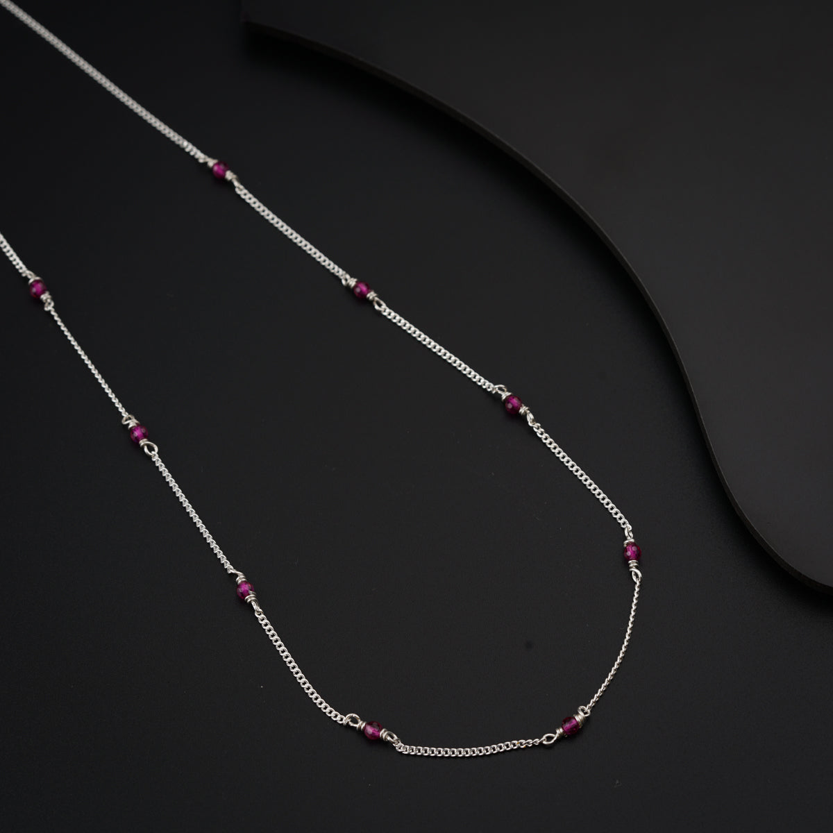 a silver chain with a red bead on it