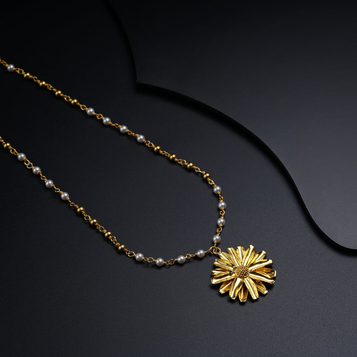 a gold necklace with a flower on a black background