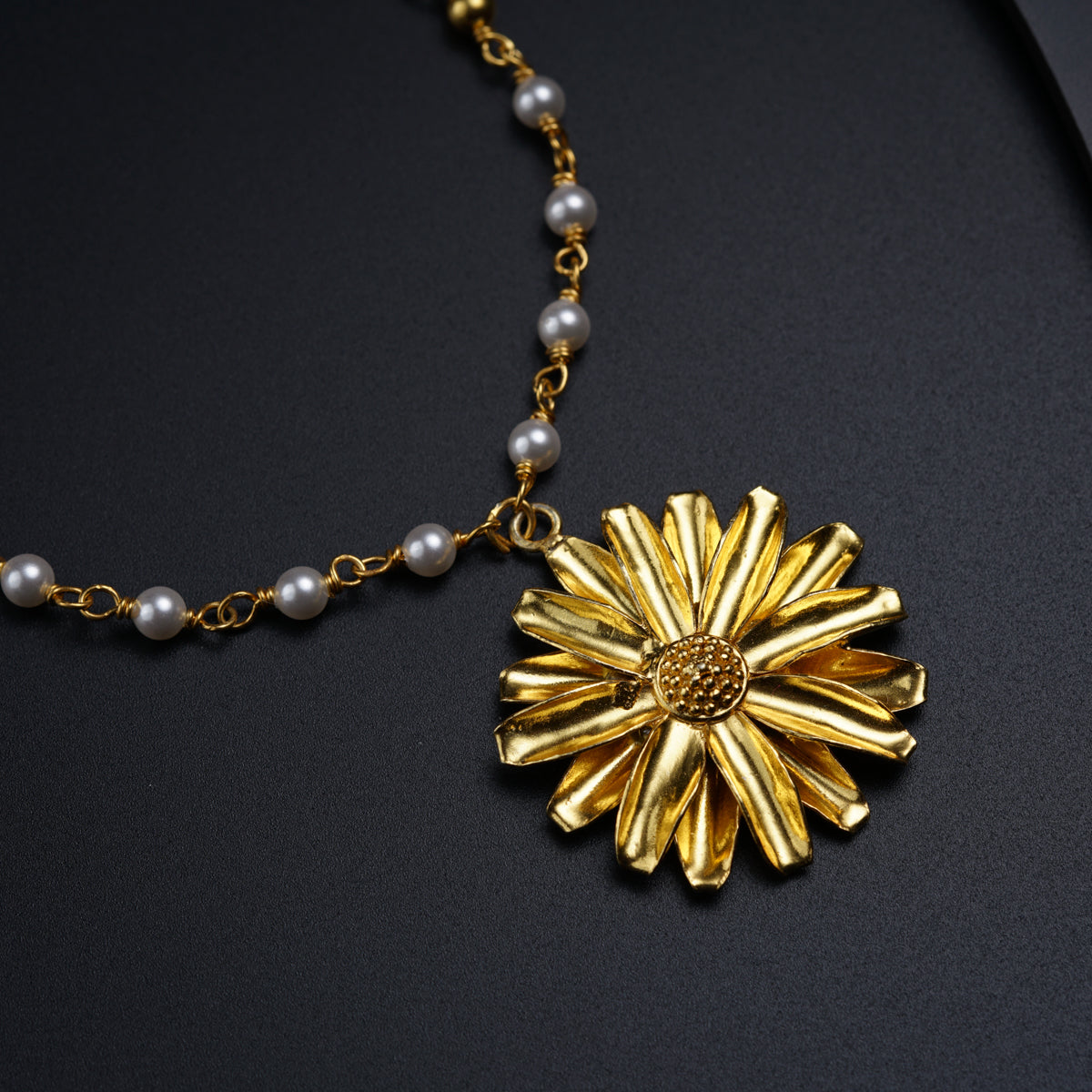 a necklace with a flower and pearls on a black surface