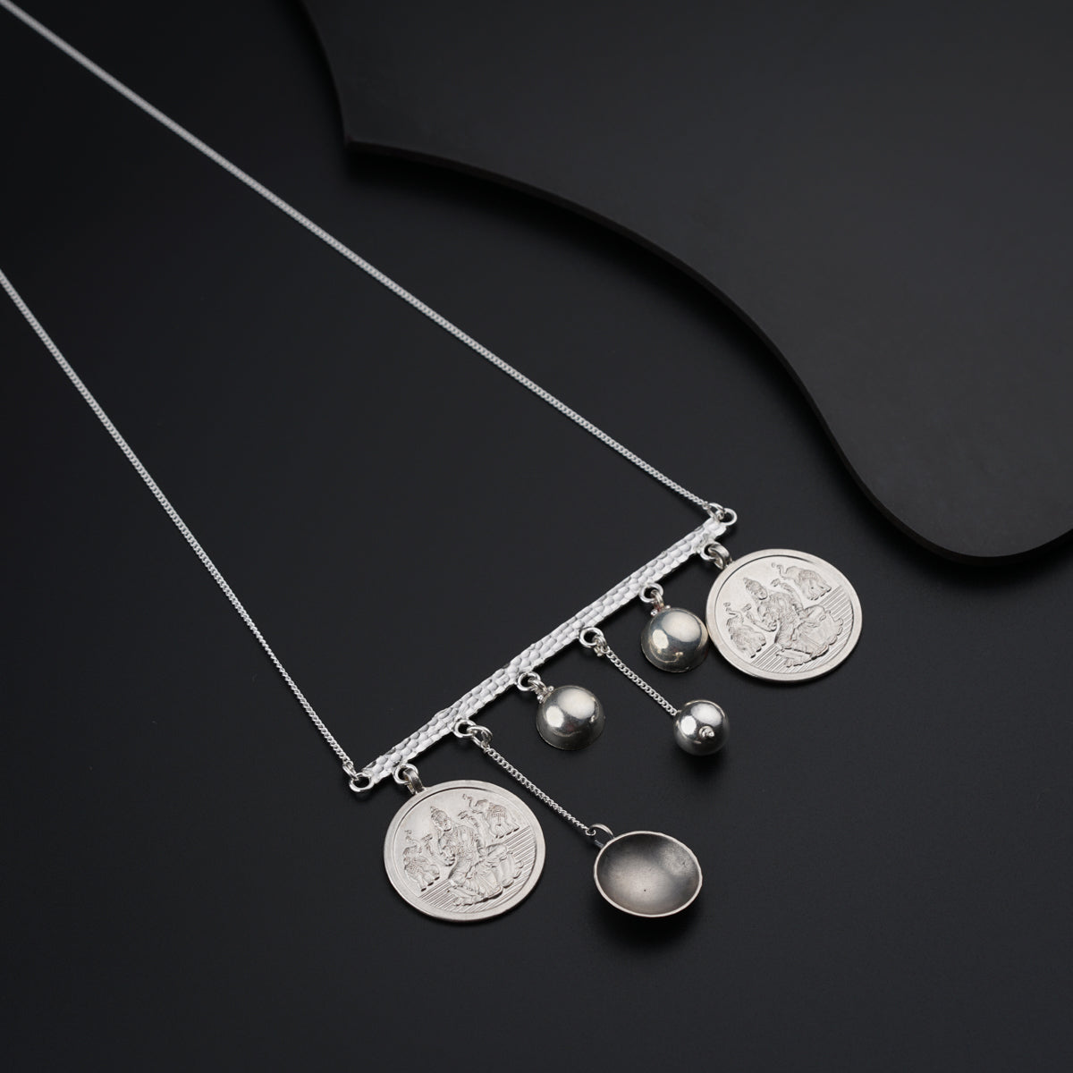 a silver necklace with a coin and three balls hanging from it