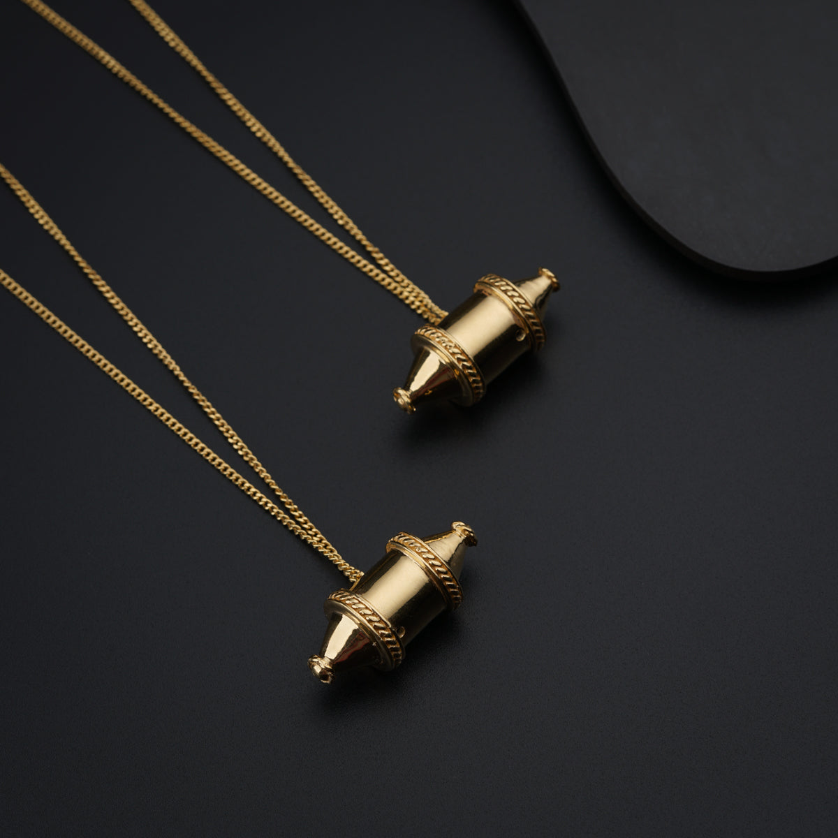 a pair of gold necklaces sitting on top of a black surface