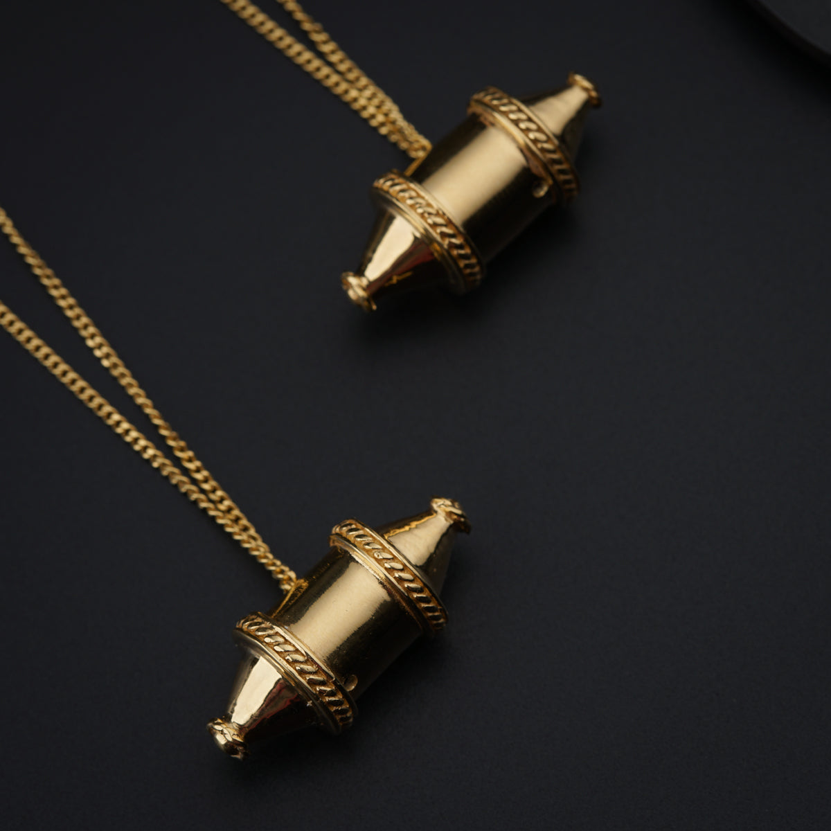 two gold necklaces on a black surface