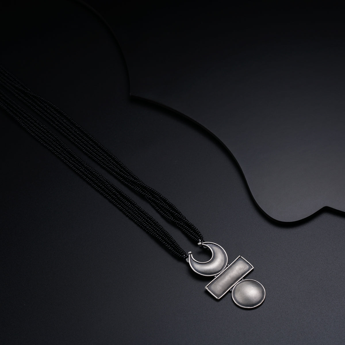 a black necklace with a silver pendant on a black background