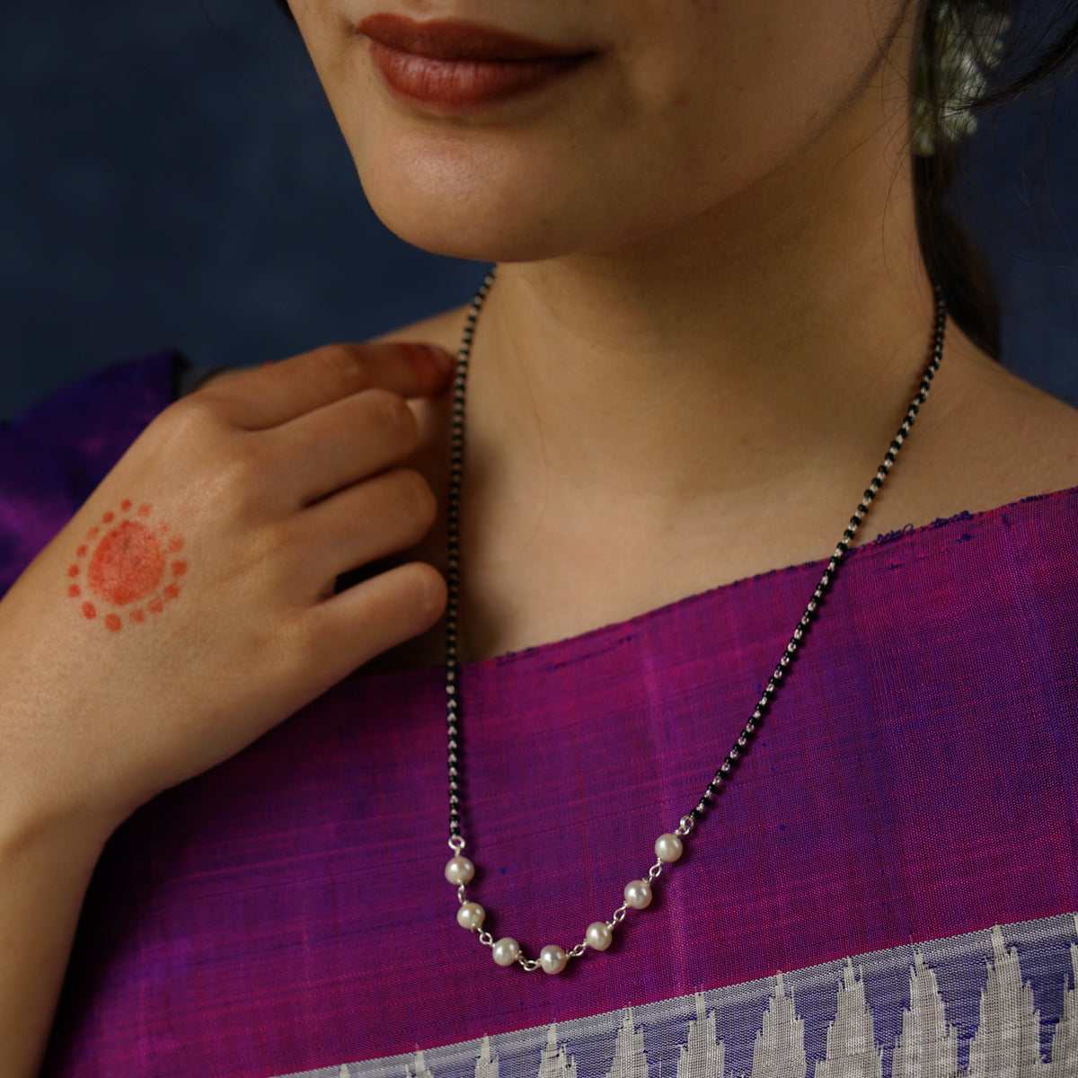 a woman wearing a necklace with a red dot on it