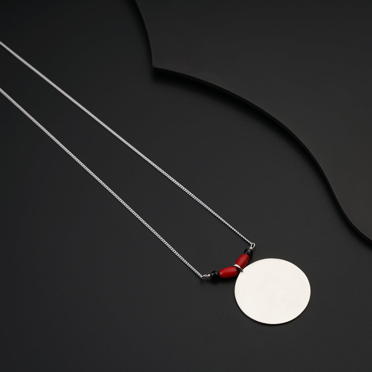 a necklace with a white disc and a red bead hanging from it