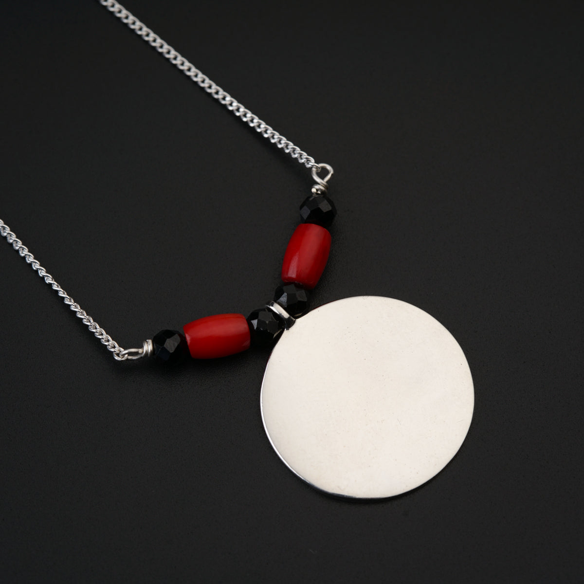 a red and black necklace with a white disc