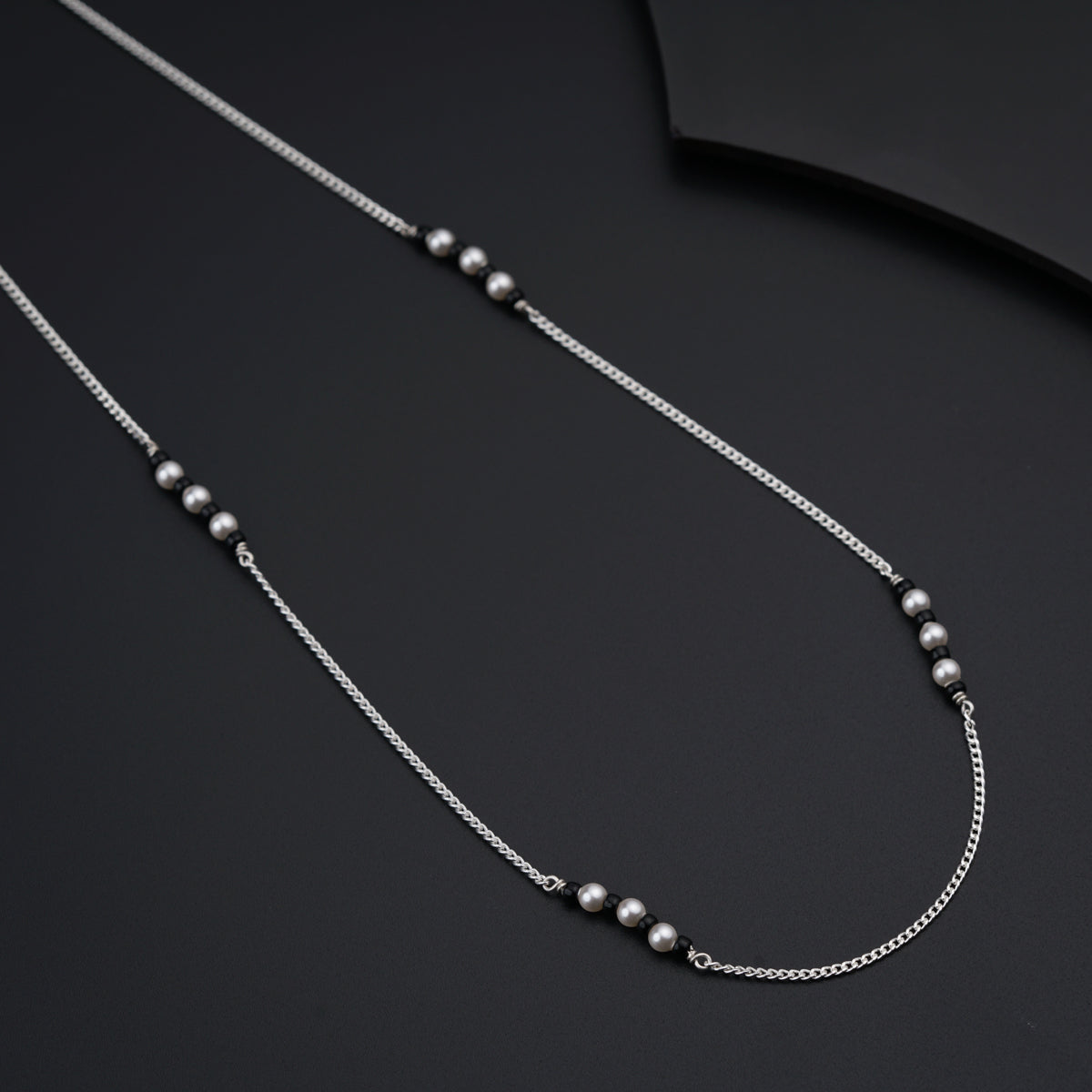 a silver necklace with beads on a black surface