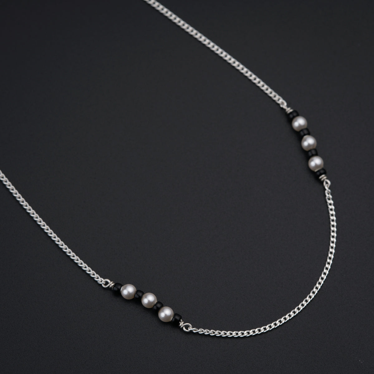 a silver necklace with pearls on a black background