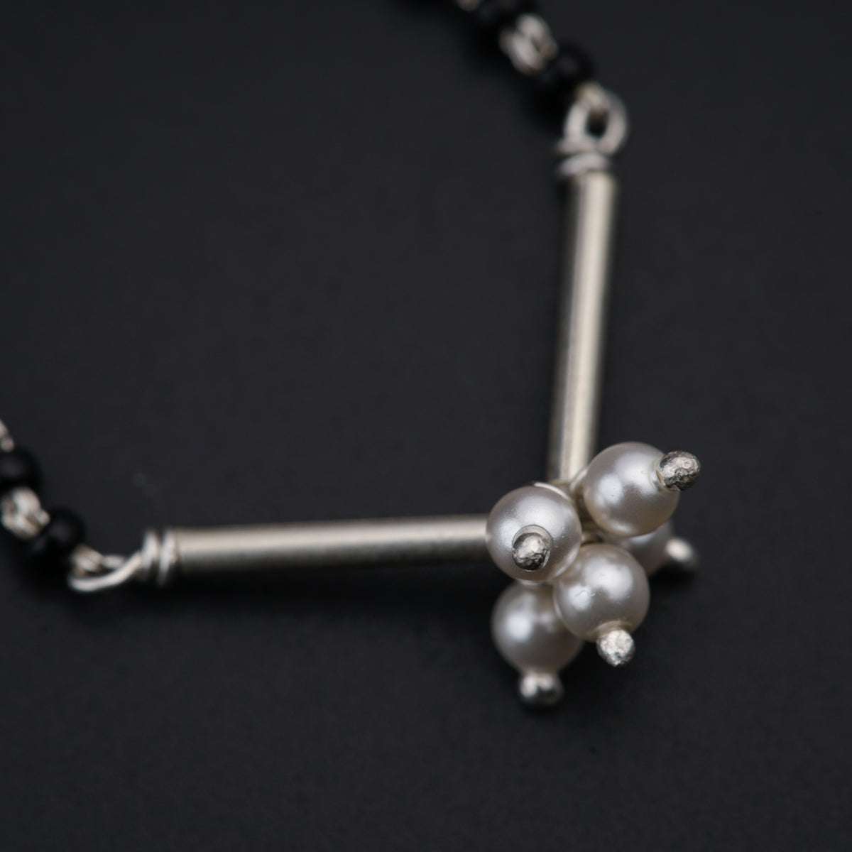 a silver necklace with pearls and beads on a black background