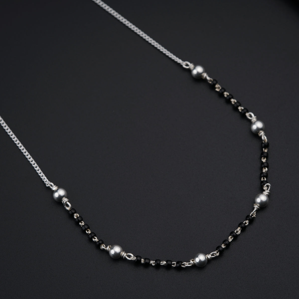 a black and silver beaded necklace on a black surface