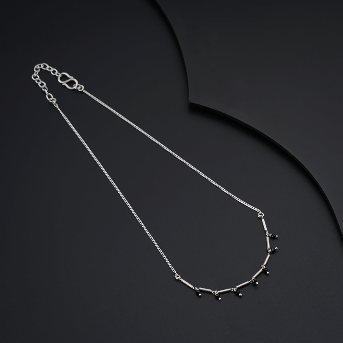 a silver necklace with black beads on a black background