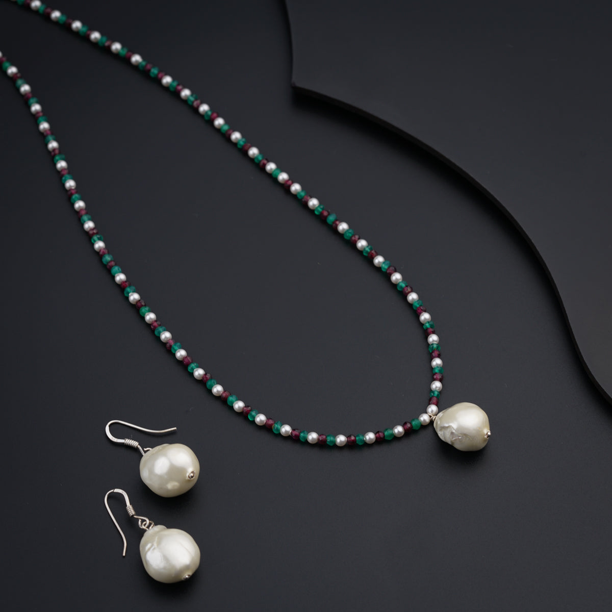 a necklace and earring with pearls on a black surface