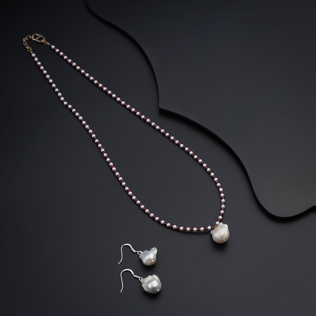 a necklace and earring with pearls on a black surface