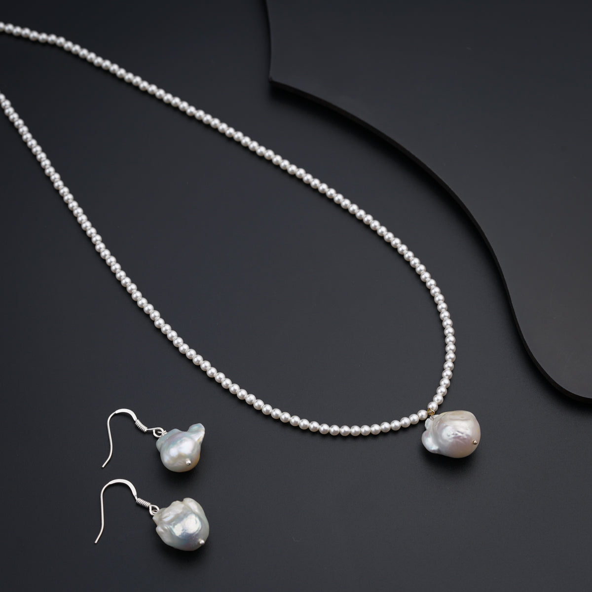 a necklace and earring with pearls on a black surface