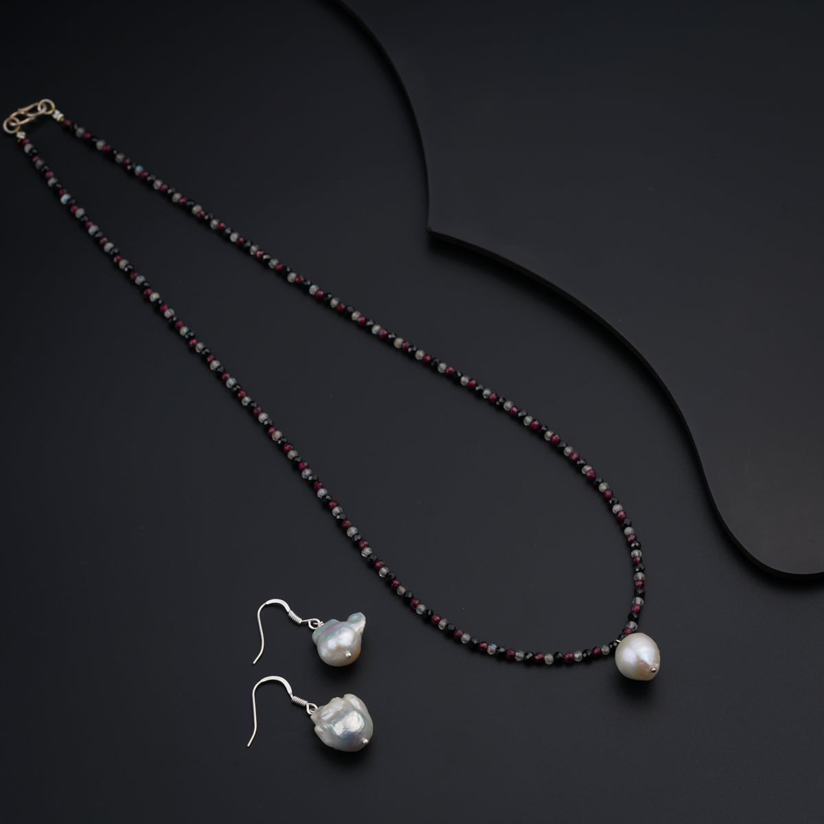 a necklace and earring with pearls on a black surface