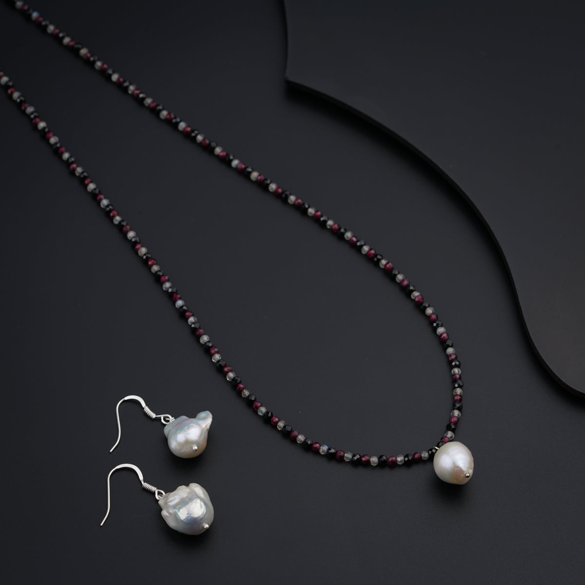 a necklace and earring with pearls on a black surface