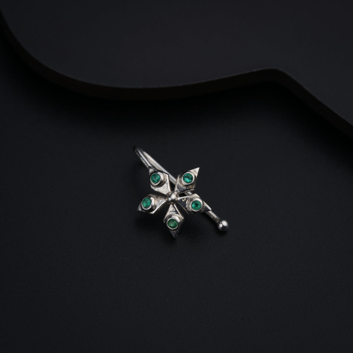 a silver brooch with green stones on a black background